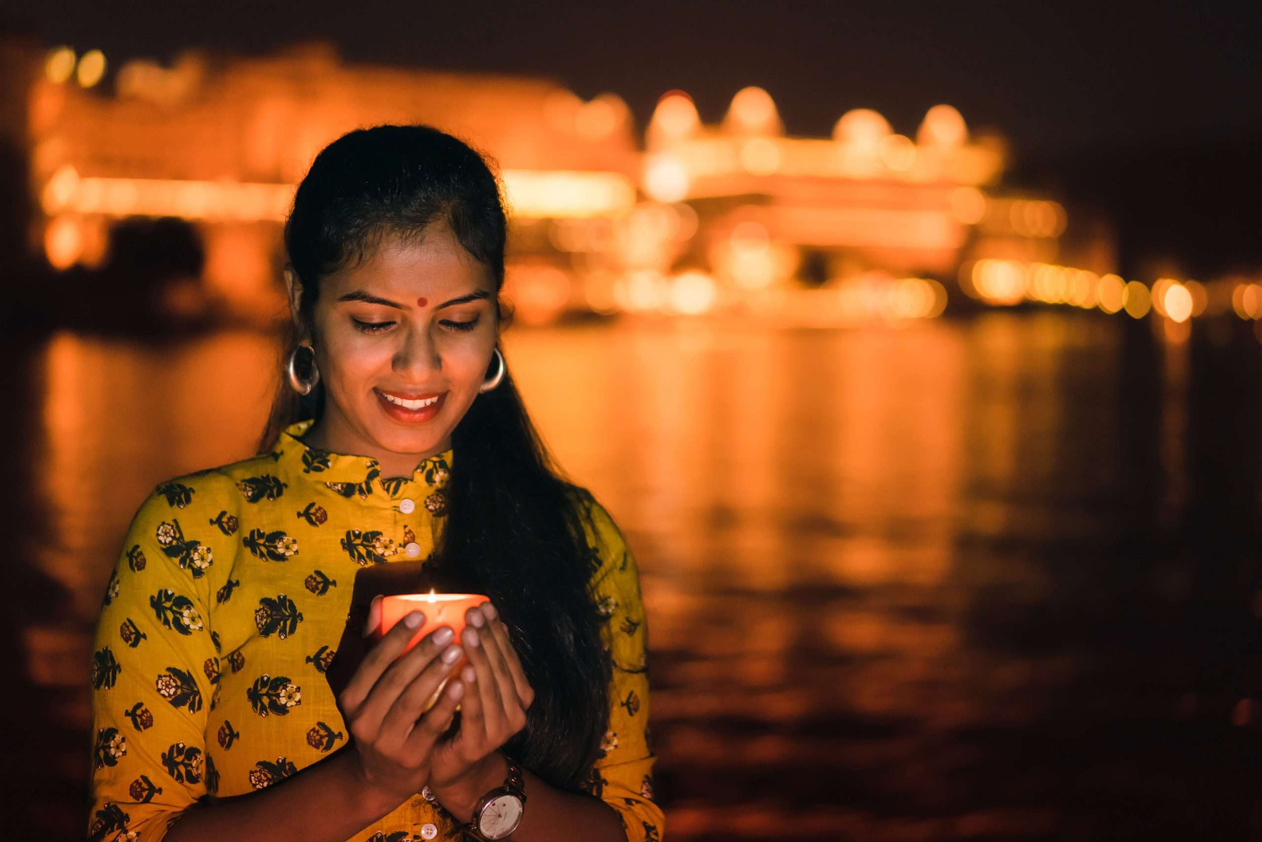 A lady lights on oil lamp by a river in Rajasthan, India.